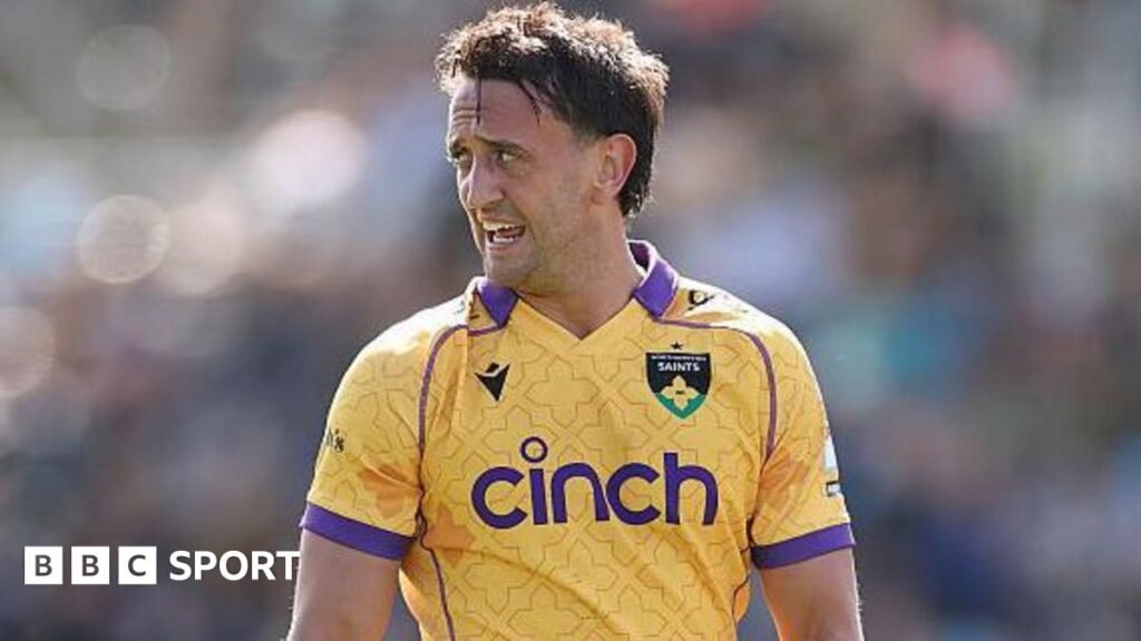 Northampton Saints rugby union player Alex Mitchell looks to his right while playing a match, wearing a yellow shirt with purple trim