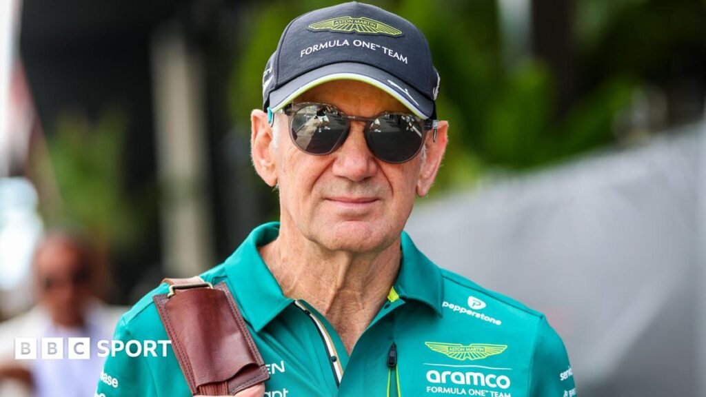Adrian Newey in the Monaco paddock wearing sunglasses, and an Aston Martin cap and green polo shirt. He is carrying a bag over his right shoulder