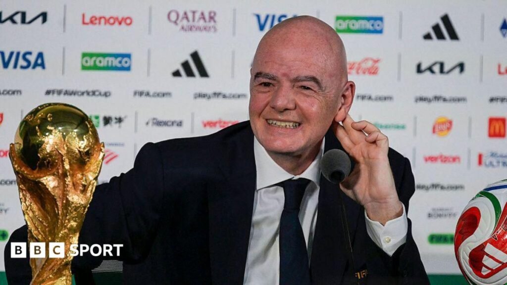 FIFA president Gianni Infantino, in dark suit and tie and white shirt, speaks next to the World Cup trophy and a football during a news conference on the eve of the opening match of the 2026 World Cup