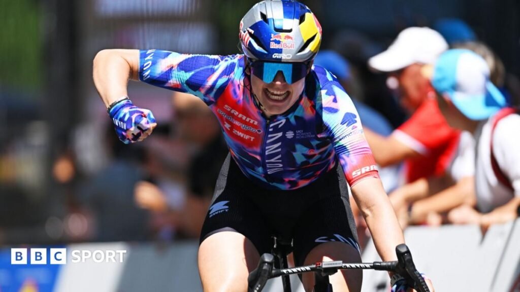 Zoe Backstedt with one hand on the handlebars punches the air with her right fist as she crosses the line