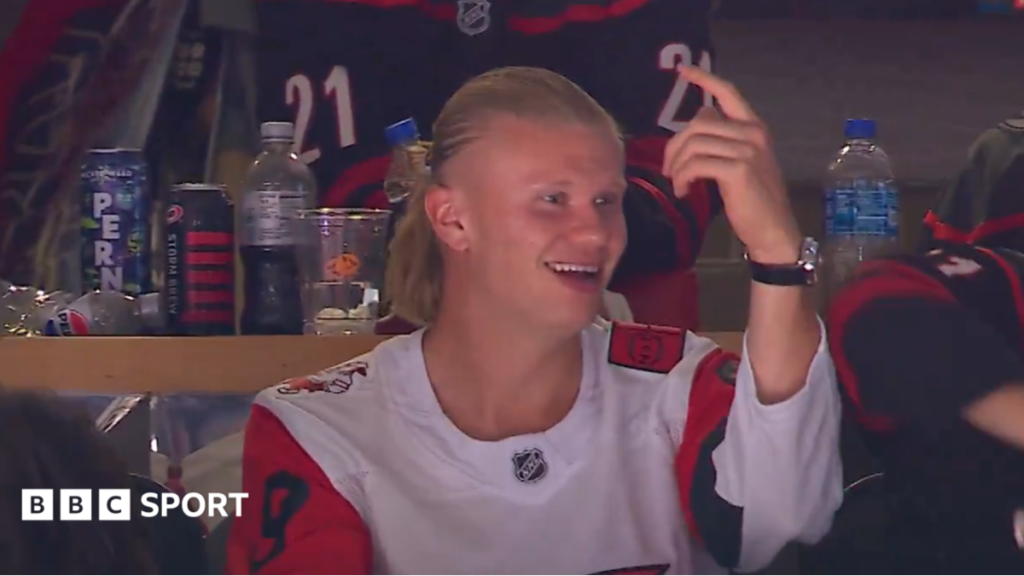 World Cup 2026: Haaland takes in ice hockey before World Cup debut Erling Haaland, wearing a white Carolina Hurricanes jersey with red, black and white sleeves, smiles and points his left hand in the air