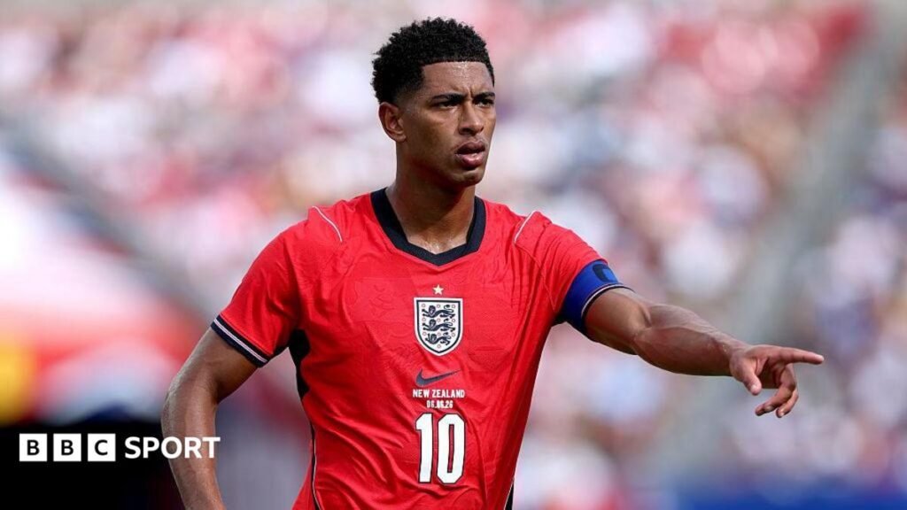 World Cup 2026: Jude Bellingham has fight to start for England – Thomas Tuchel Jude Bellingham, wearing a red England shirt with a white number 10 in the centre beneath the badge, extends his left arm and points his index finger