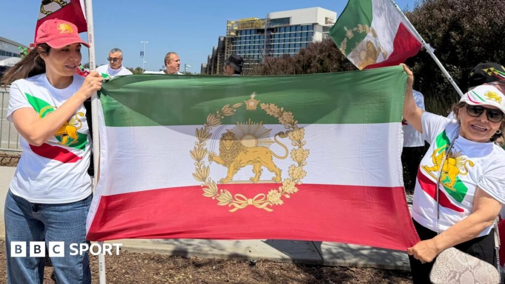 World Cup 2026: The flag Iranians are not allowed to wave at stadiums Two women wear t shirts and caps featuring the stylised lion symbol of the flag of Iran's pre-1979 Islamic revolution. They are also holding the flag between them.