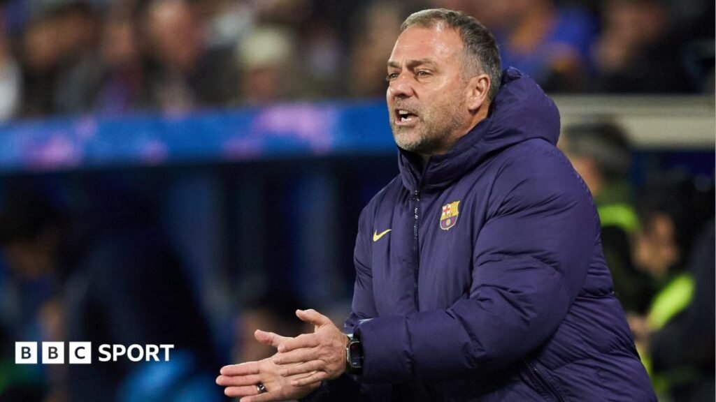 Hansi Flick, wearing a blue padded Barcelona club coat, stands in the touchline, applauding