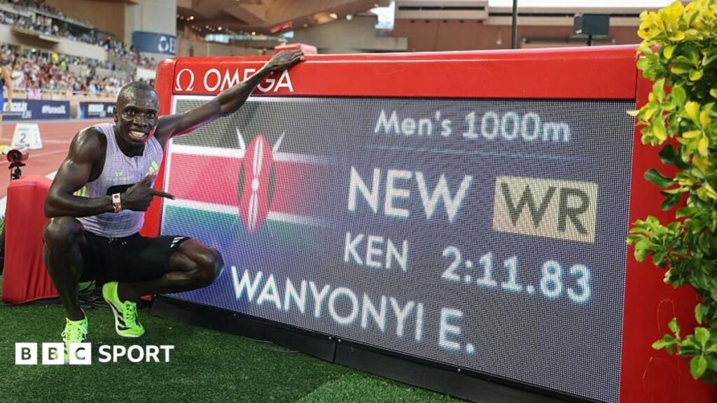 Emmanuel Wanyonyi poses for a photograph next to a digital screen showing his name and world record time after winning the 1,000m in Monaco