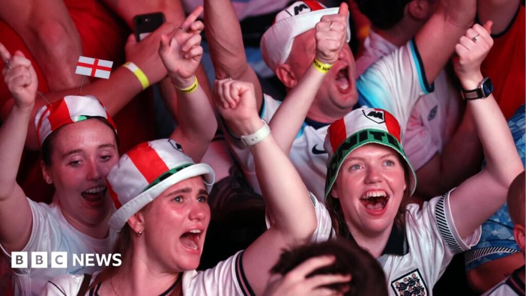 England fans dressed in red and white hats celebrate with their arms raised during a World Cup match.
