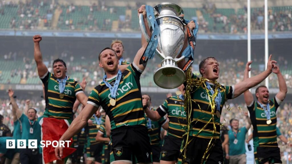 Fraser Dingwall (left) holds the Prem trophy aloft in his left arm and Fin Smith (right) holds it in his left, with his right arm held up to his side and finger pointing. The pair are walking on the pitch at the Allianz Stadium with their mouths open after winning the Prem final