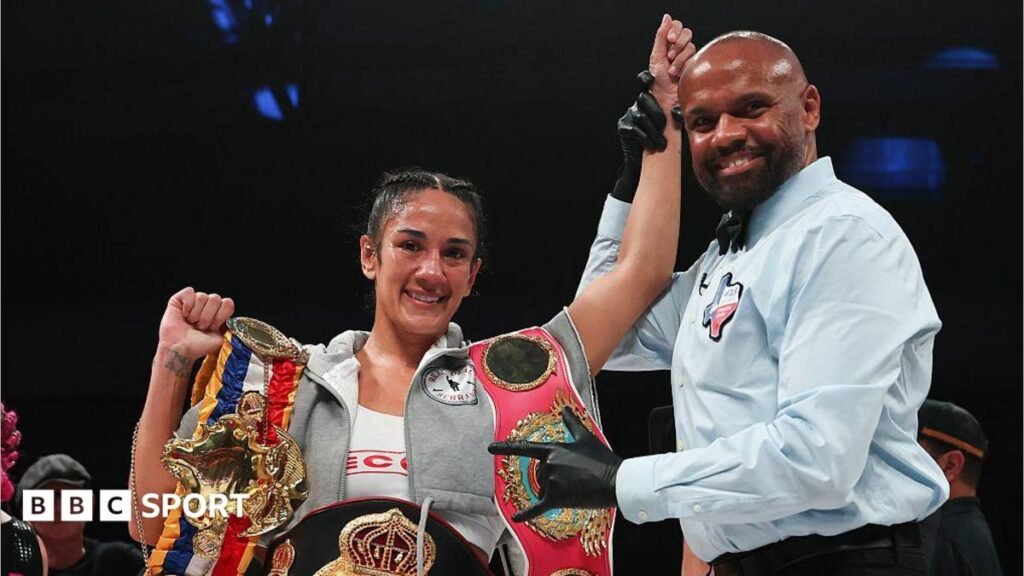 Amanda Serrano has her arm raised by a referee and is celebrating with her belt