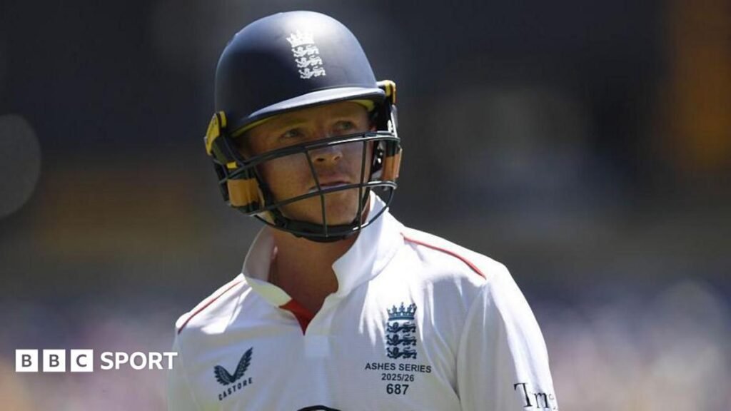 Ollie Pope, wearing a blue helmet and white England shirt, looks to his left
