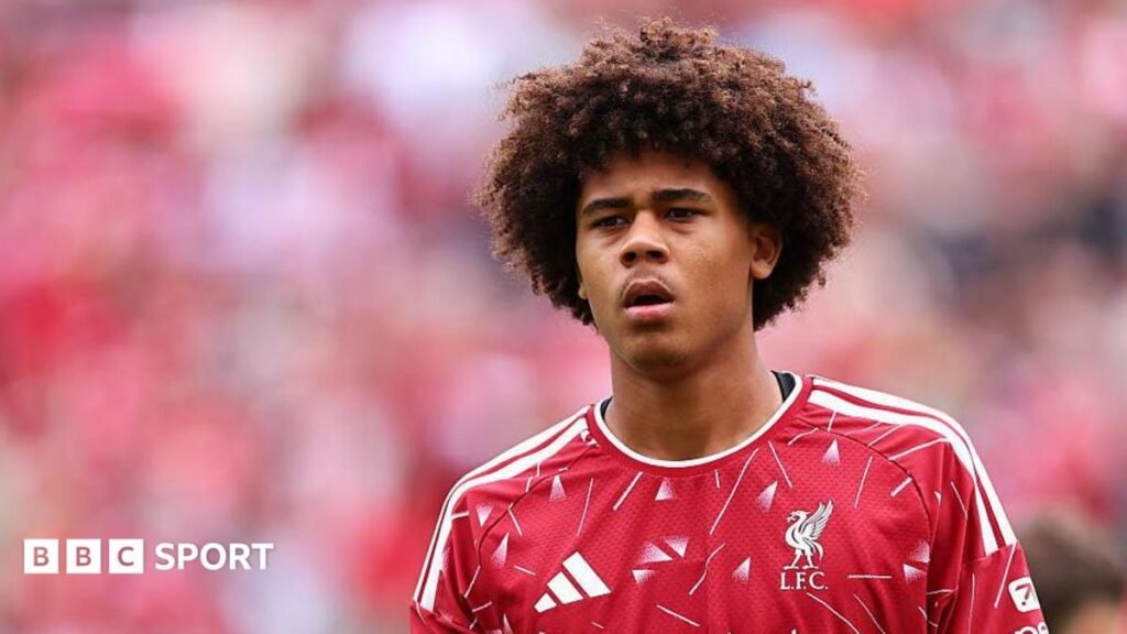 Ifeanyi Ndukwe is looking on in a red Liverpool shirt