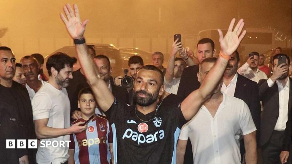Mohamed Salah: Turkish club Trabzonspor set to sign former Liverpool forward Mohamed Salah with a black Trabzonspor top on with his hands in the air outside Trabzon airport