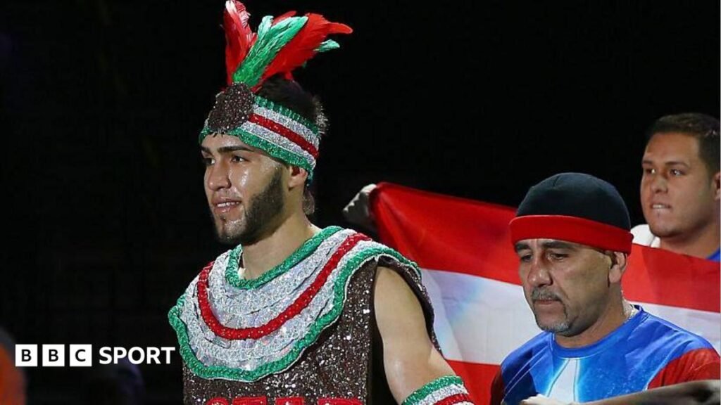 Prichard Colon wears a sparkly red, silver and green vest and headband with feathers