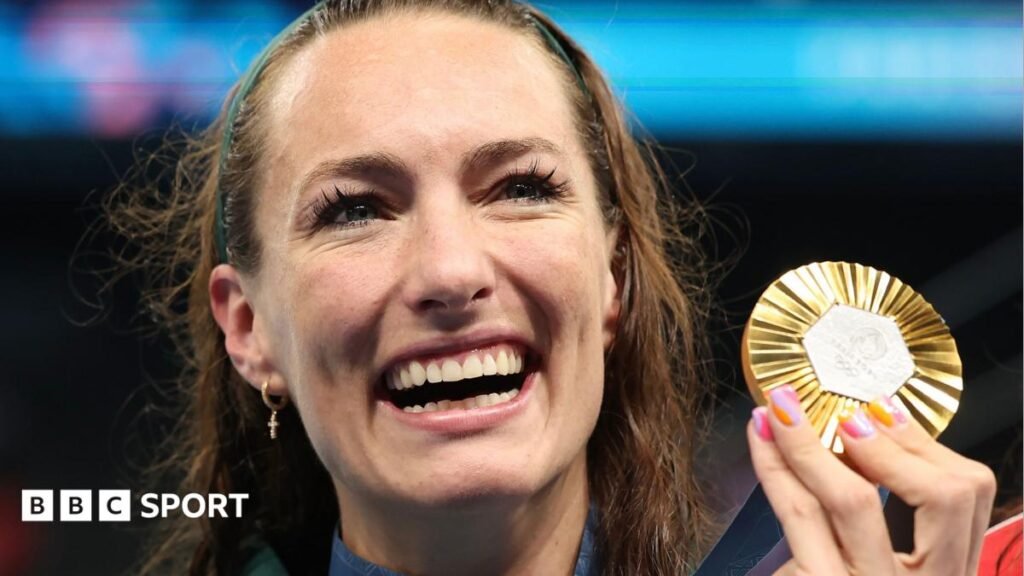 Tatjana Smith: South African swimmer comes out of retirement Tatjana Smith, wearing dark green South Africa tracksuit bottoms and shortsleeved training top, smiles as she kneels on a large raised stage and holds up a South African flag to her right. The swimmer also has an Olympic gold medal on a ribbon around her neck. A large crowd of people can be seen gathered around the stage, with some leaning over barriers at the front and others seated in gently sloping stands, while in the background the Eiffel Tower rises directly behind Smith into a blue sky dotted with white-grey clouds