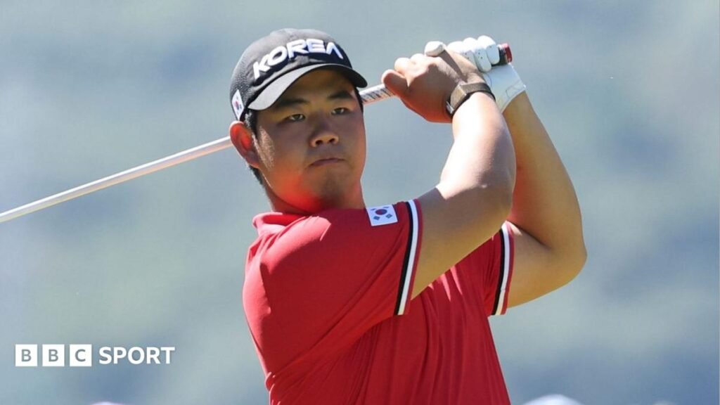 2026 Asian Games: Tom Kim leads men’s golf event seeking win to secure military service exemption Tom Kim in a red polo shirt and a black cap, both featuring badges with the flag of South Korea. His club is behind his head at the conclusion of his swing