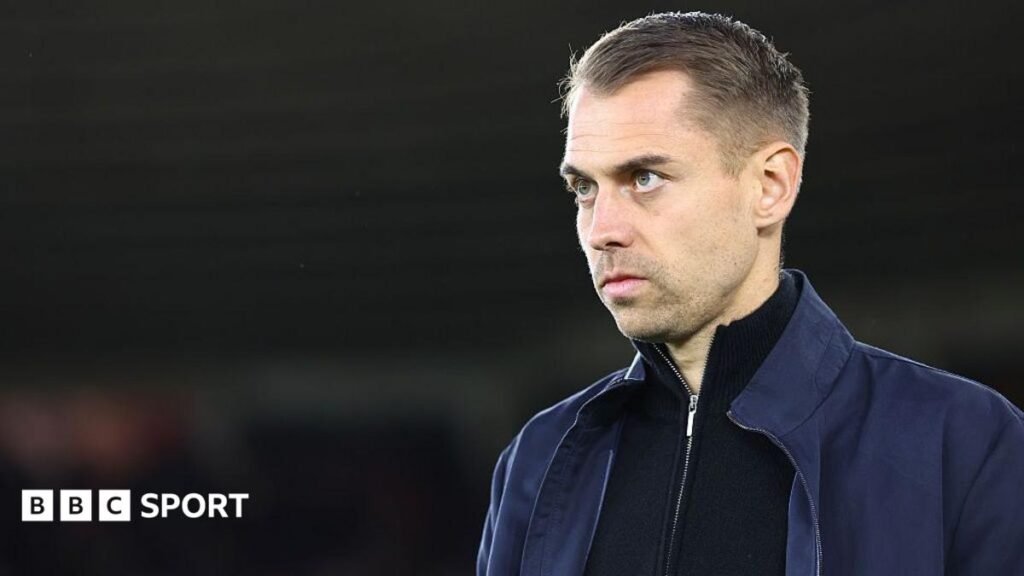 Spygate: Southampton manager Tonda Eckert given suspended ban A man in a dark jacket and blue jeans stands partially concealed by a tree trunk and holds a phone up in two hands as if filming and has a white earphone in his right ear