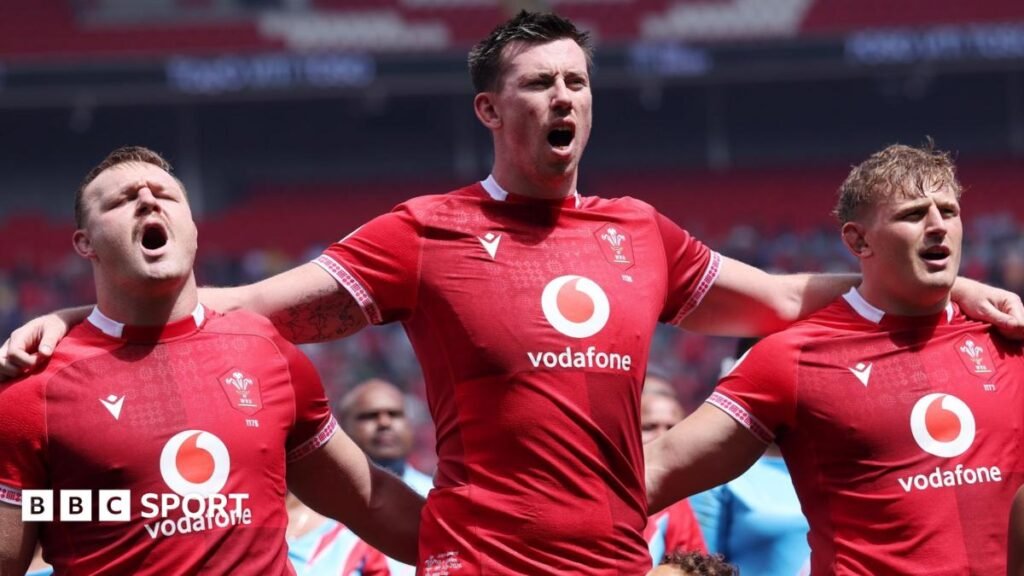 Adam Beard in the centre has his arms around the shoulders of Dewi Lake and Jac Morgan as the three Wales players in red jerseys sing the national anthem before a game.